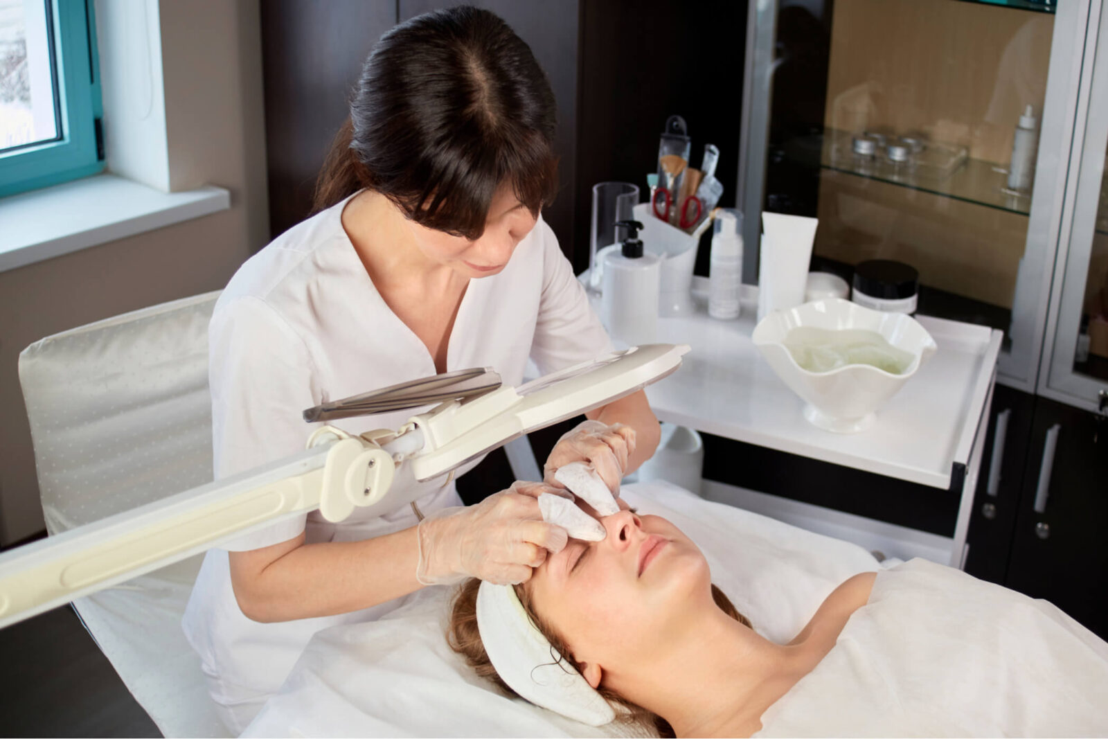 A cosmetologist cleanses the skin of a female client from black spots