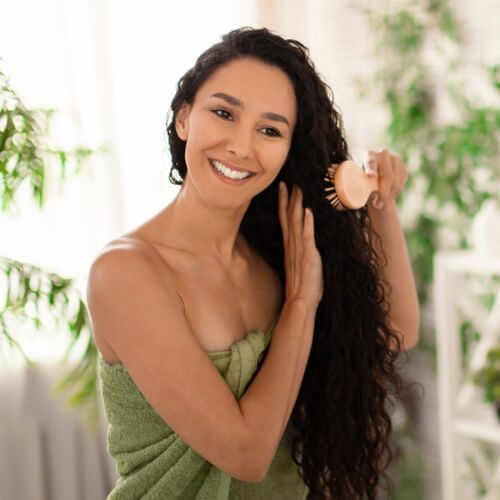 Pretty happy young woman in towel brushing her wavy long hair